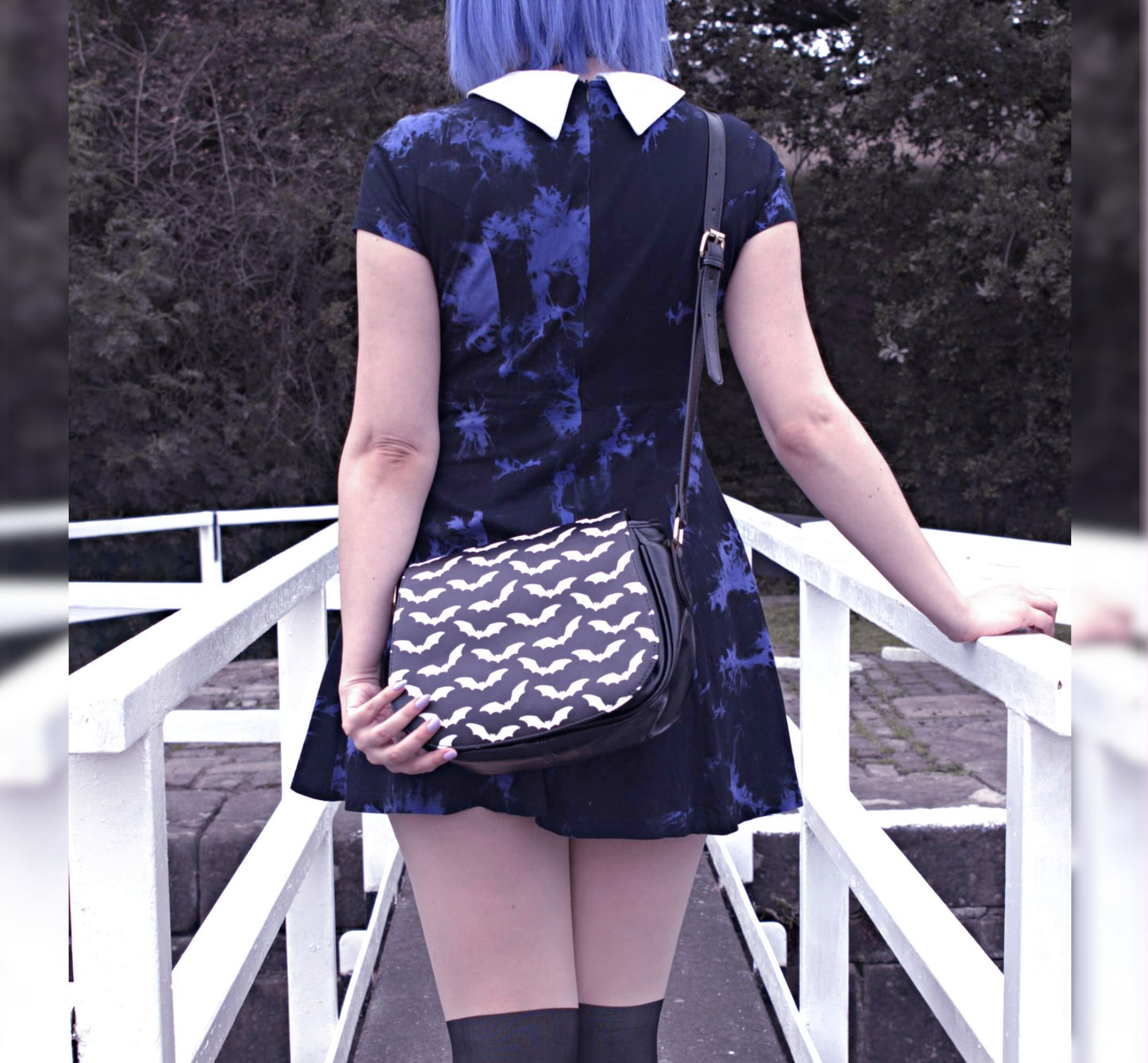 Person wearing a blue dress with a bat bag on a white railing.