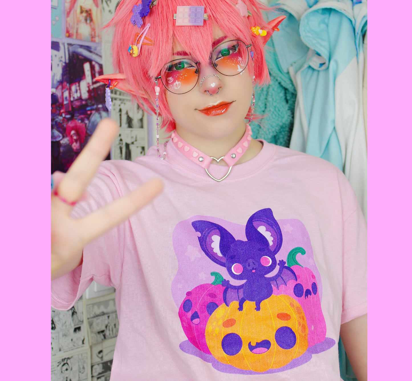 Person wearing a pink t-shirt with a colorful Halloween graphic design, posing in a room with pink walls.