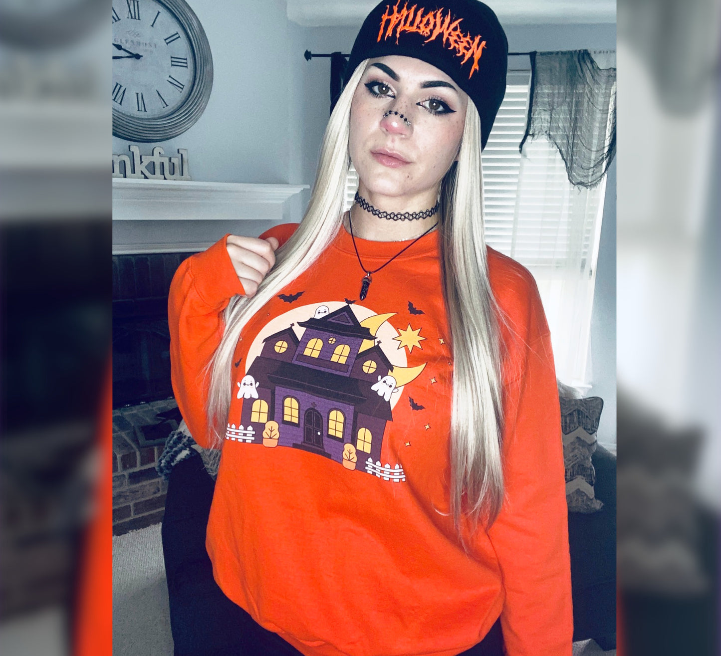 Person wearing an orange Halloween-themed sweatshirt and black cap indoors.