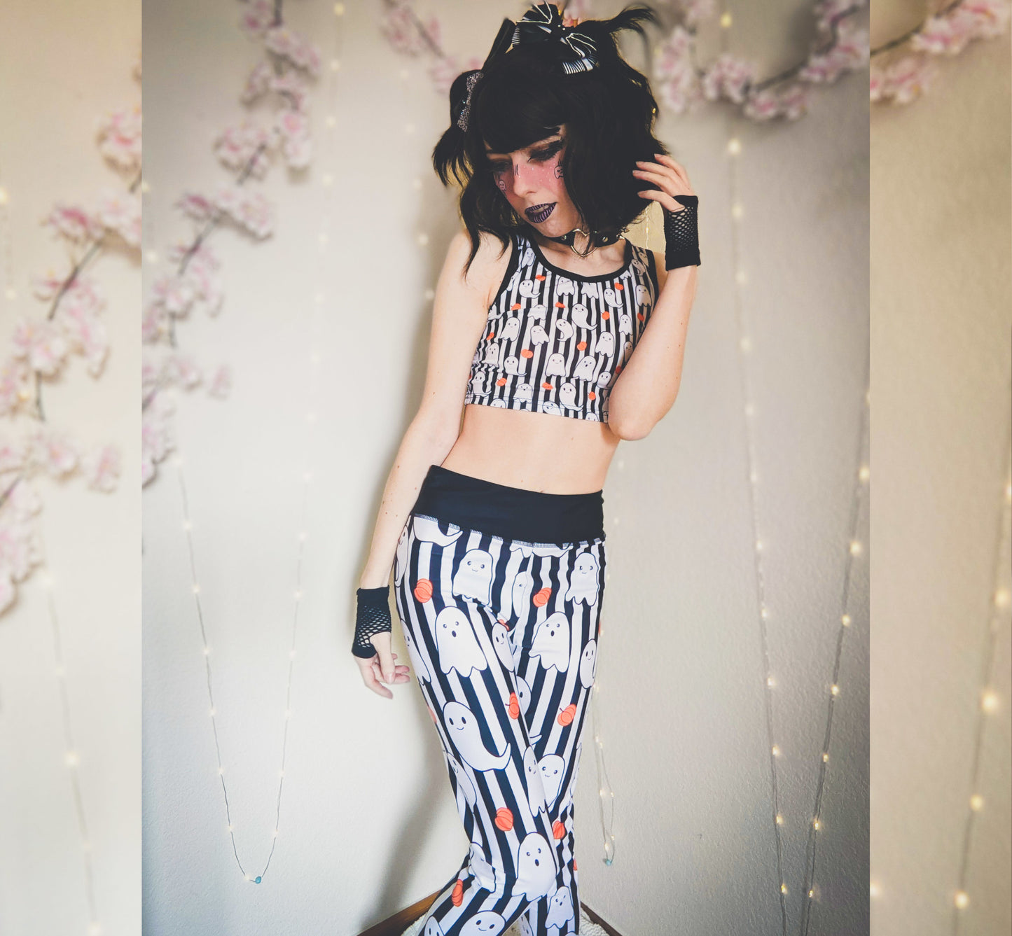 Girl wearing a black and white patterned outfit with ghost design, standing against a floral and string light background.
