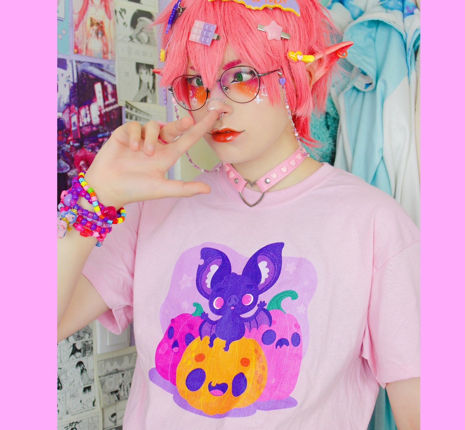 Person with pink hair and colorful accessories wearing a pink t-shirt with a cut bat design.