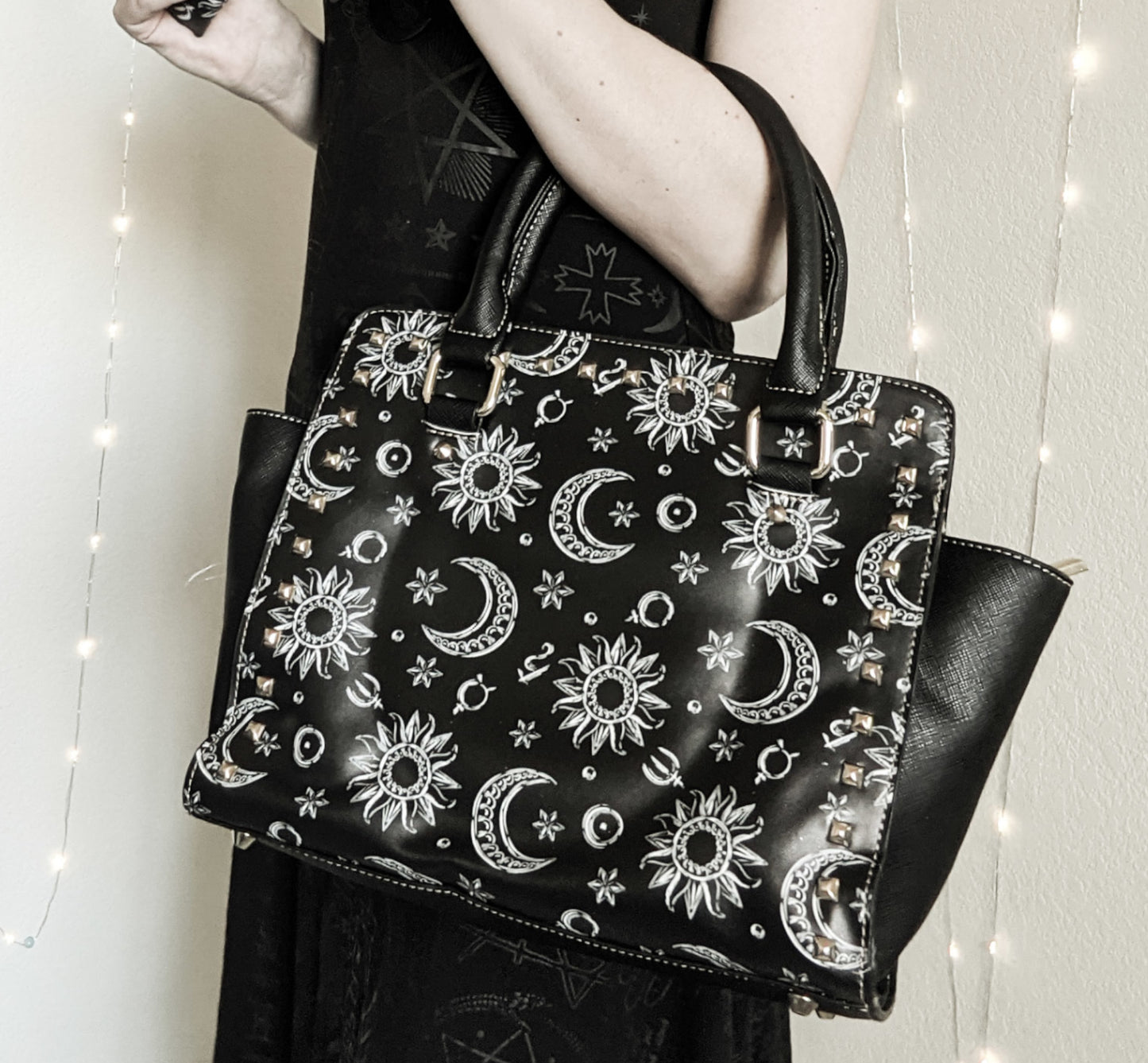 Black handbag with celestial pattern held by a person against a neutral background