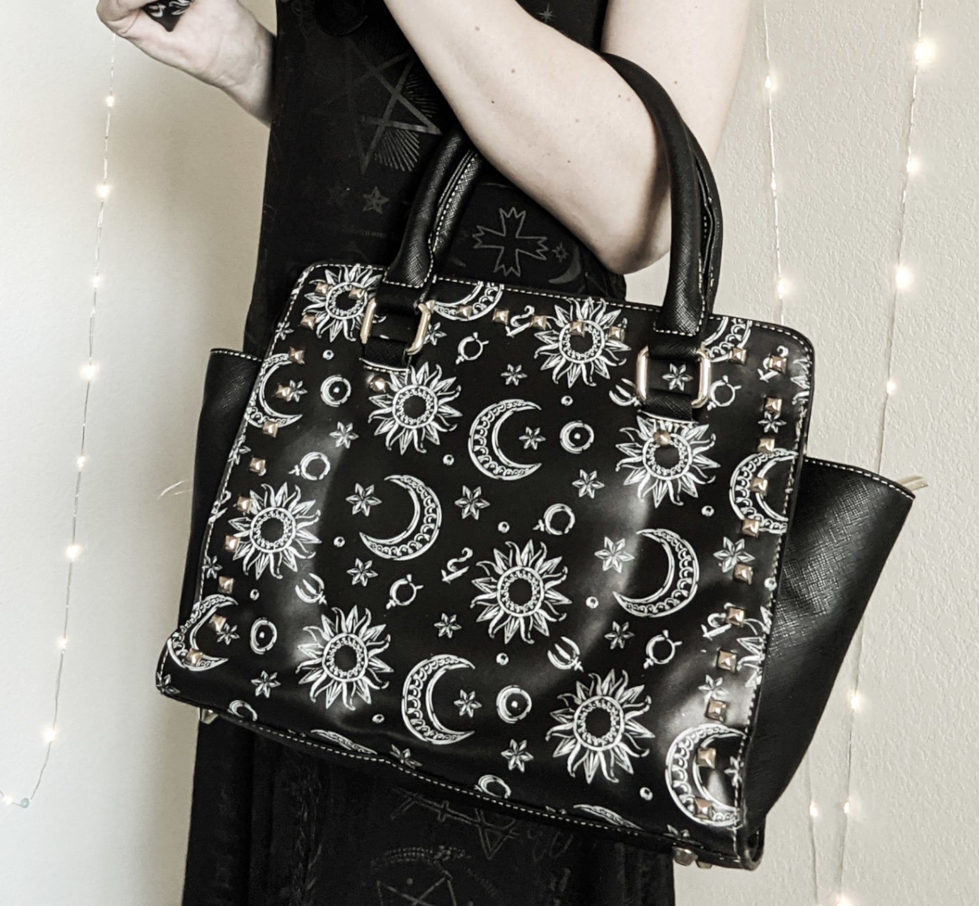 Black handbag with celestial pattern held by a person against a neutral background