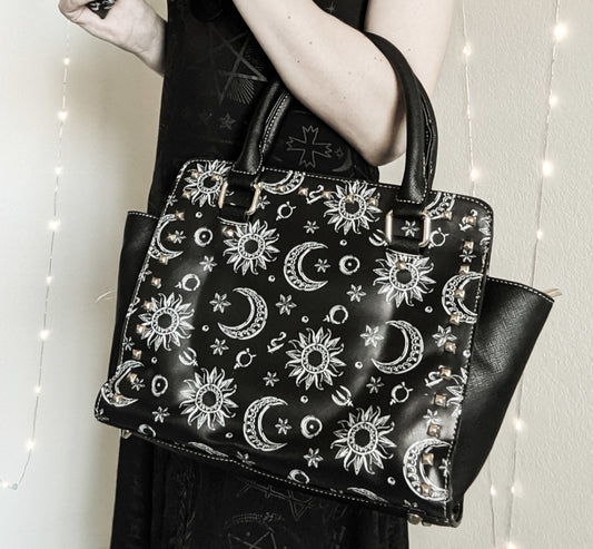 Black handbag with celestial pattern held by a person against a neutral background